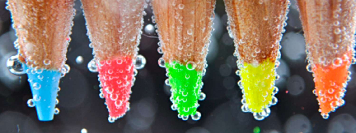 Das Bild zeigt fünf Farbstifte unter Wasser mit Blasen
